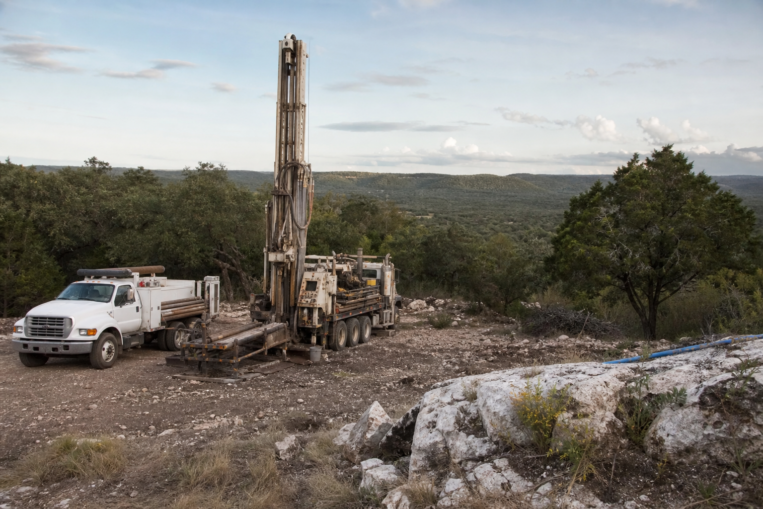 Blanco County Texas rural drilling site with water well rig and service truck on rocky Hill Country acreage